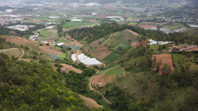 Aerial view of a mountain valley with farmlands and cloudy sky in Constanza, Dominican Republic. Scenic rural landscape with forested hills.