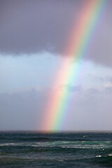 A huge rainbow connects with the horizon over a dark blue stormy ocean. 