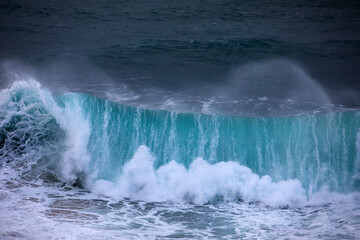 A huge turquoise ocean wave folding and exploding into a violent wall of white water during a storm...