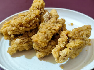 A plate of crispy golden fried chicken fillet, served on a blurred background.
