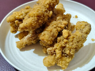 A plate of crispy golden fried chicken fillet, served on a blurred background.