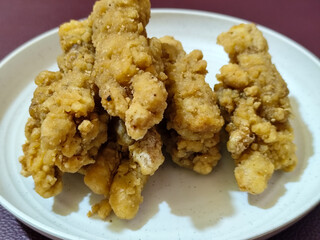 A plate of crispy golden fried chicken fillet, served on a blurred background.