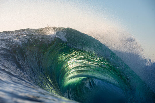 A beautifully vibrant backlit emerald coloured glassy surfing wave breaking over a shallow reef. Captured from the ocean's surface on sunrise. - Powered by Adobe