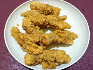 A plate of crispy golden fried chicken fillet, served on a blurred background.