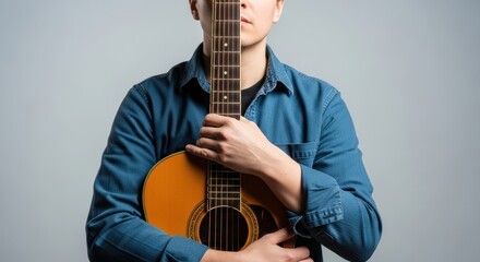 Obraz premium Young asian male holding acoustic guitar against chest wearing blue shirt