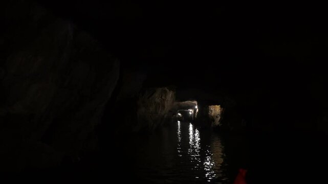 Boat navigating underground river through Trang An Grotto, revealing geological wonders and hidden natural landscape in dark subterranean environment