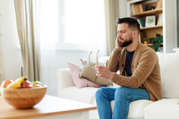 Young Man Holding Glasses While Sitting on Sofa in Well-Lit Living Room Experiencing Discomfort