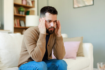 Obraz premium Young Man Experiencing Pain at Home While Sitting in a Cozy Living Room