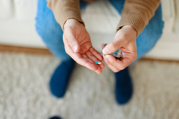 Close-Up View Of Hands Holding Medicine Pills While Wearing Beige Sweater And Blue Jeans At Home