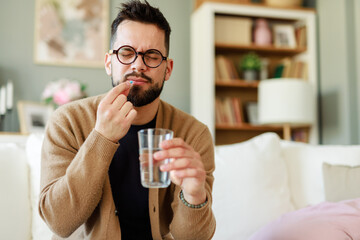 Caucasian Man in Glasses Taking Medicine While Sitting in a Comfortable Living Room