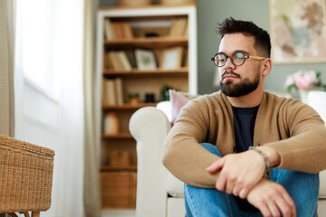 Young Caucasian Man in Living Room Sitting Thoughtfully Amid Cozy Decor and Soft Natural Lighting