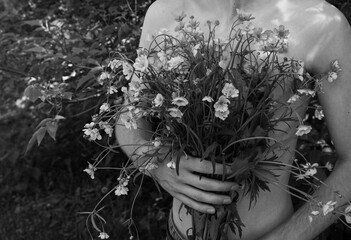 A shirtless person holds a bouquet of wildflowers close to their chest