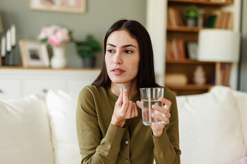 Young Woman Holding Pill and Glass of Water in a Cozy Living Room Setting