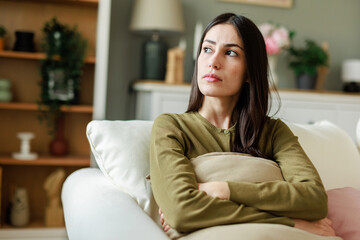 Young Caucasian Woman Sitting on Couch Holding Pillow in a Thoughtful Expression at Home