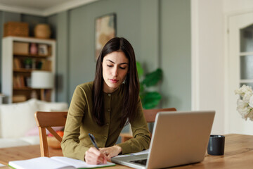 Young Woman in Green Shirt Working From Home Using a Laptop and Notebook in a Comfortable Indoor Space