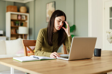 Young Woman in Green Shirt Experiencing Pain While Working from Home in a Bright, Modern Interior