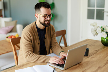 Smiling Young Caucasian Man Working on Laptop in a Bright Modern Home Environment