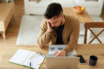 Caucasian Young Man Working from Home in Pain at Wooden Table with Laptop and Documents