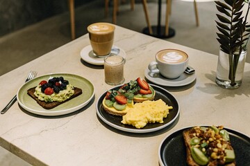 A brunch table with avocado toast, pancakes with berries, scrambled eggs, and two lattes