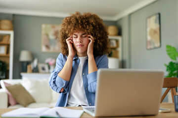 Obraz premium Young Woman with Curly Hair Struggling with Headache While Working from Home at a Desk