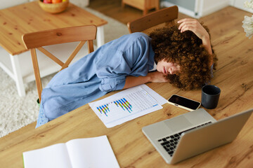 Young Woman with Curly Hair in Pain Resting on Desk While Working from Home
