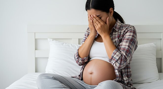 Pregnant woman in distress sitting on a bed covers face with hands - Powered by Adobe