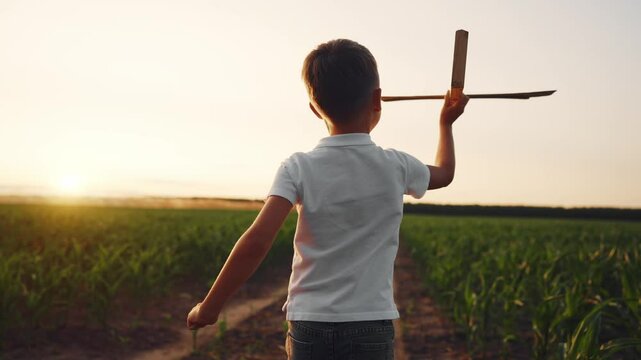 Little boy running in countryside and holding wooden plane in hands, back view. Happiness and joy, child dreaming about future choose of professional occupation and hobby, slow motion shot, childhood