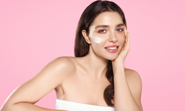 Wellness and beauty, non invasive facial treatment concept. Beautiful young model, woman applies moisturising cream, nourishing her face with daily routine skincare products, pink background