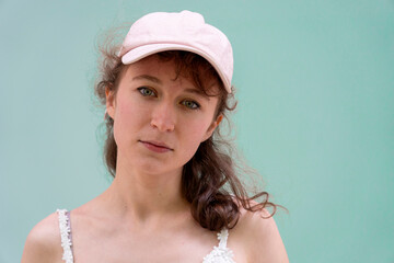 A stylish woman wearing a pink cap poses against a soft mint background, embodying contemporary...