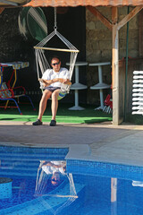 Man in a swing chair by a swimming pool