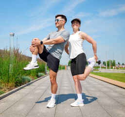 Fitness enthusiasts engage in dynamic stretching on a sunny day in a modern urban park while...