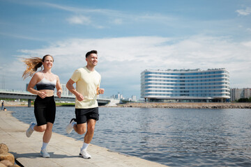 Fototapeta premium Couples jog along a riverside promenade under clear blue skies, enjoying the revitalizing morning energy of the city