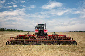 Rear view of a large tractor with a plow standing in a field. Start tillage after harvest.