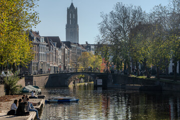 Sunny autumn view along Utrecht’s Oudegracht. People relax on the wharf as a pedal boat drifts...