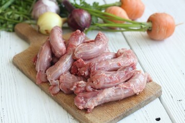 Raw chicken necks on a cutting board. Fresh baby carrots, onions and garlic on a white wooden table.