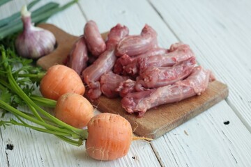Raw chicken necks on a cutting board. Fresh baby carrots, onions and garlic on a white wooden table.