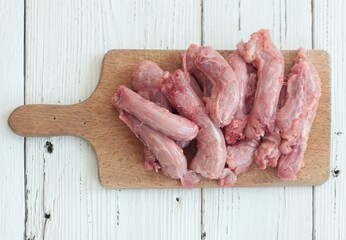 Raw fresh chicken necks on a cutting board.  Chicken neck meat flat lay on white wooden table.