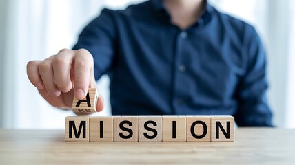 Wooden blocks spelling out mission with a hand adding a letter letters word