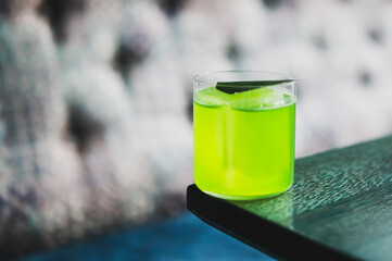 Green cocktail with ice and garnish served in a clear glass on a dark wooden table, with a blurred background. Refreshing summer drink close-up.