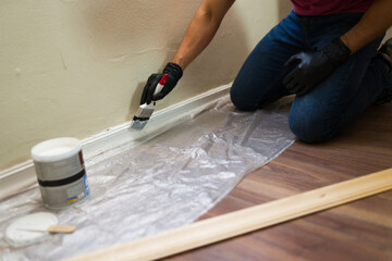 Contractor painting skirting board with white paint during home renovation