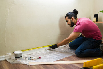 Male Latin contractor measuring wall using tape measure for home renovation