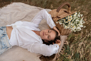 Picnic Daisies Woman: Young woman relaxes on blanket during daytime picnic with flower-filled basket.