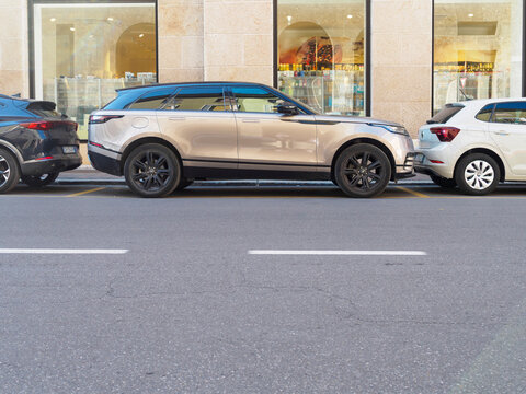 Silver Range Rover Velar parking between black SUV and white hatchback, highlighting urban automotive space constraints and sleek vehicle styling