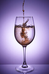 Glass of sparkling drink with splash on purple background
