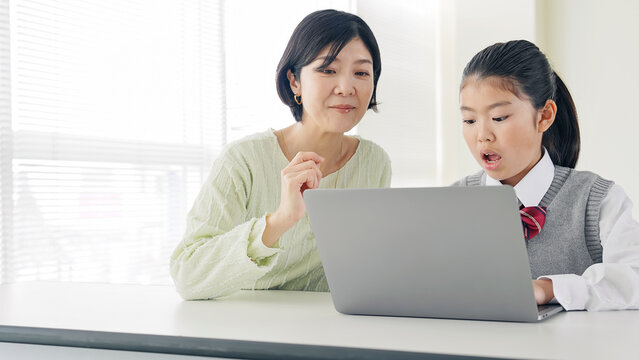 教室で女性教員からパソコンを教わる女の子 - Powered by Adobe