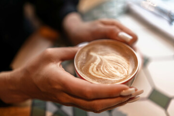Coffee Hands Latte held indoors, warmth, relaxation, enjoyment during day at cafe, latte art visible.