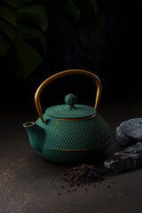 Green cast iron teapot with gold handle on dark background