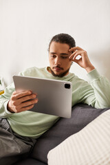 Engaging young man relaxing at home while using a tablet for entertainment and information