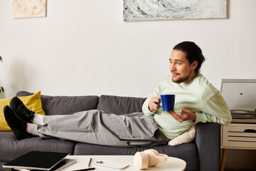 Relaxing at home, a young man enjoys a cozy afternoon with a warm beverage in hand
