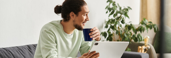 Young man enjoying coffee while using a tablet in a cozy home environment during morning hours